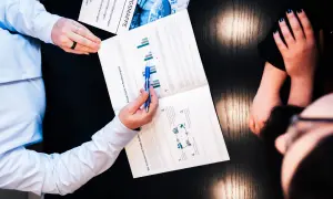 Zwei Personen besprechen ein Dokument über Private Equity und Rendite. Ein Mann zeigt mit einem Stift auf Diagramme.