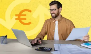 Mann am Schreibtisch mit Laptop und Papieren, Euro-Symbol und Pfeile im Hintergrund. Erklärt, was ist ein Verrechnungskonto.
