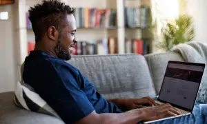 Mann auf Sofa nutzt Laptop, um mit umfragen geld verdienen steuer.