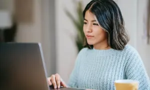 Junge Frau schreibt am Laptop eine Rechnung als Privatperson. Sie trägt einen hellblauen Strickpullover.