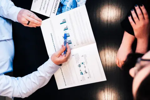 Zwei Personen besprechen ein Dokument über Private Equity und Rendite. Ein Mann zeigt mit einem Stift auf Diagramme.