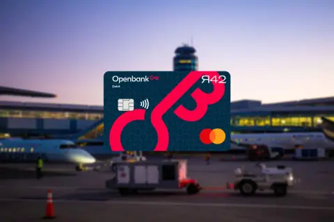 Openbank Debitkarte mit Mastercard-Logo vor einem Flughafen bei Dämmerung. Gute Openbank Erfahrungen für Reisen.