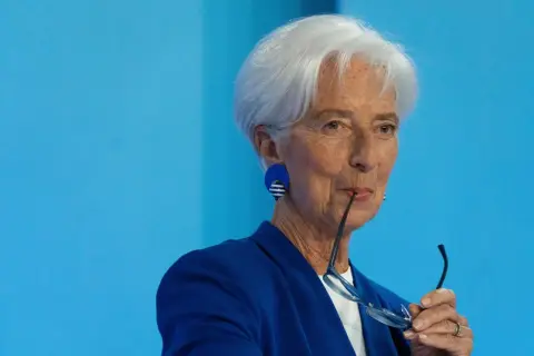 Christine Lagarde mit Brille im Mund, nachdenklich vor dem Hintergrund des EZB-Zinsentscheids.