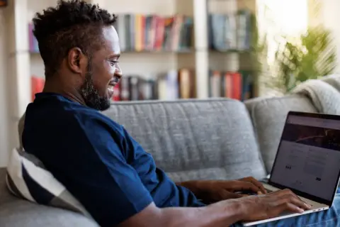 Mann auf Sofa nutzt Laptop, um mit umfragen geld verdienen steuer.