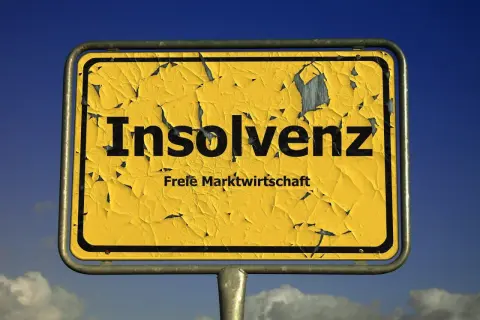 Gelbes, verwittertes Ortsschild mit der Aufschrift "Insolvenz" und "Freie Marktwirtschaft". Es fragt: was ist Insolvenz?