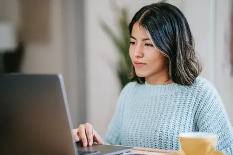 Junge Frau schreibt am Laptop eine Rechnung als Privatperson. Sie trägt einen hellblauen Strickpullover.