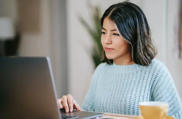 Junge Frau schreibt am Laptop eine Rechnung als Privatperson. Sie trägt einen hellblauen Strickpullover.